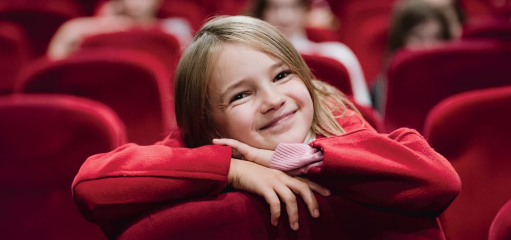 uśmiechnięta dziewczyna w czerwonej bluzsce siedząca na czerwonym fotelu kinowym na sali kinowej